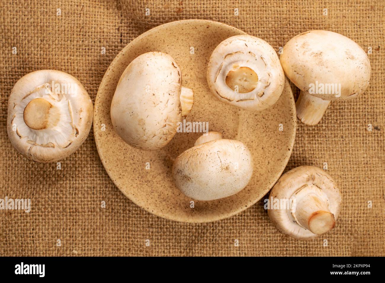 Alcuni funghi champignon freschi e freschi, con un piattino in ceramica, su un tovagliolo di iuta, vista dall'alto. Foto Stock