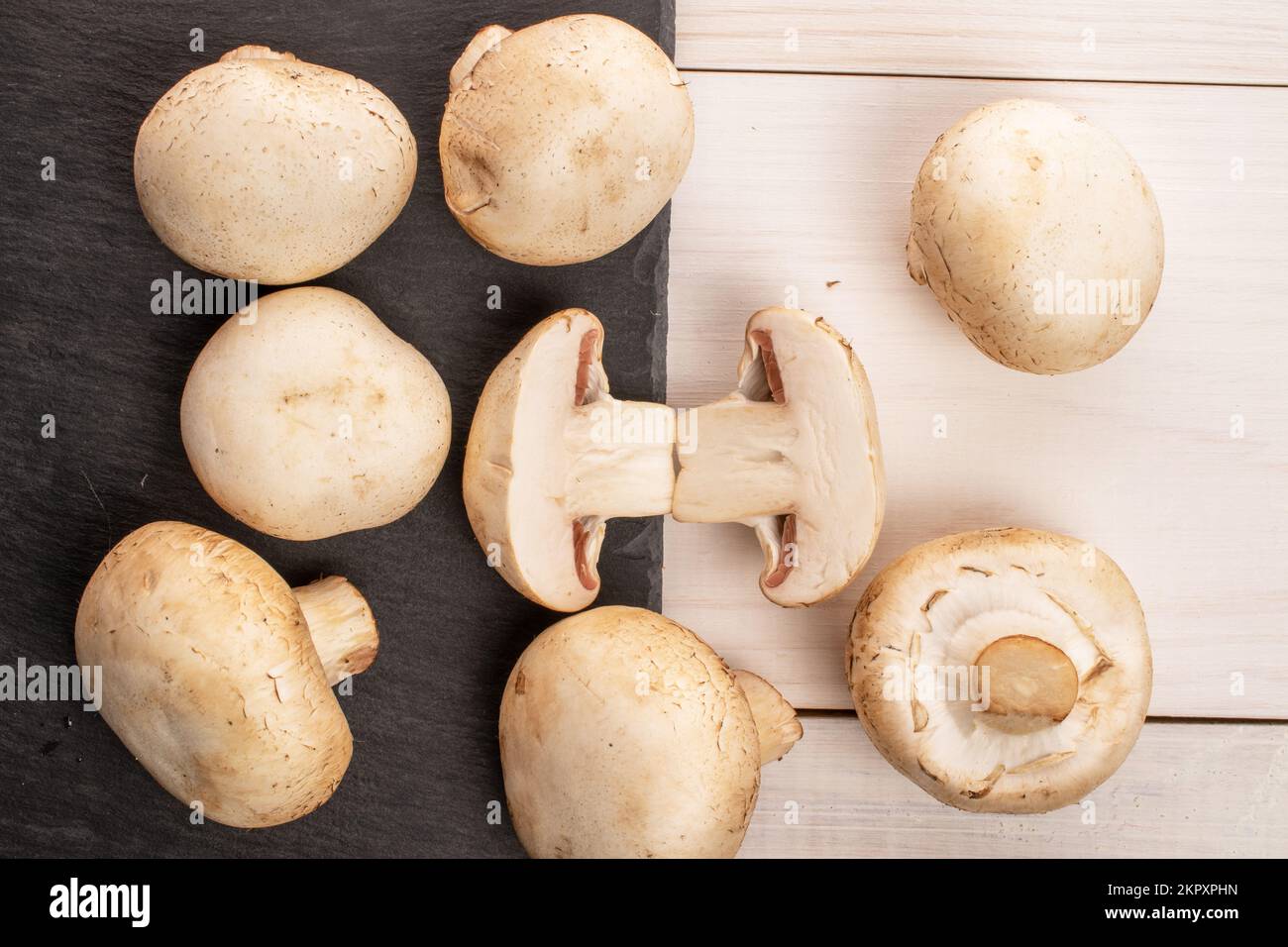 Qualche intera e due metà di appetitoso fresco biologico funghi champignon con una tavola di servizio di ardesia su un tavolo in woo naturale dipinto di bianco Foto Stock