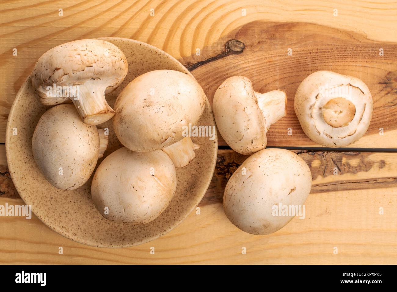 Diversi funghi freschi e appetitosi champignon interi con piattino in ceramica, su un tavolo in legno, vista dall'alto. Foto Stock