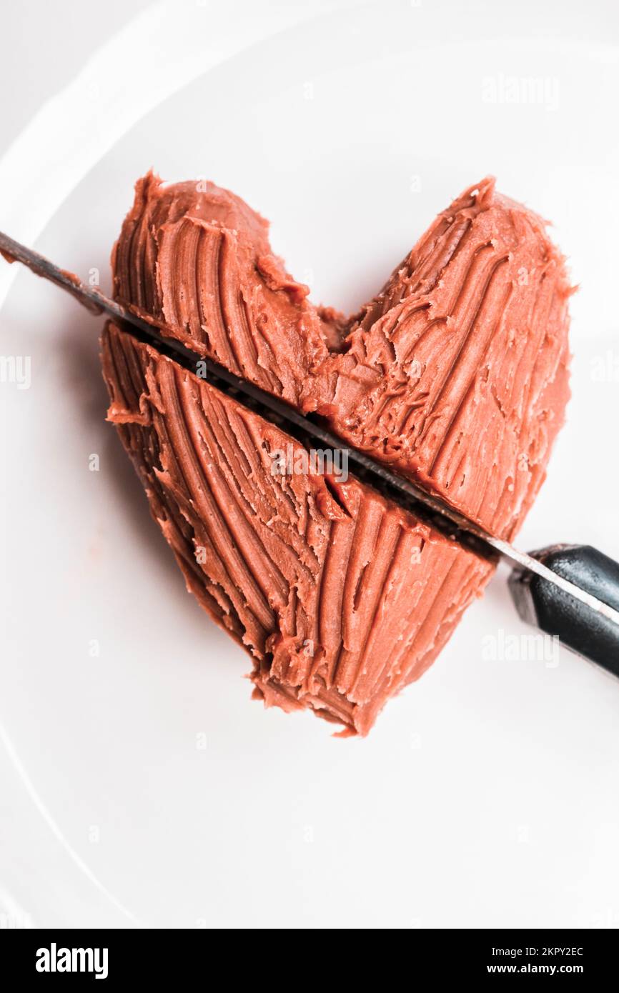 Primo piano del dolce al cioccolato a forma di cuore con taglio a coltello su un piatto bianco. Mangia il tuo cuore fuori Foto Stock