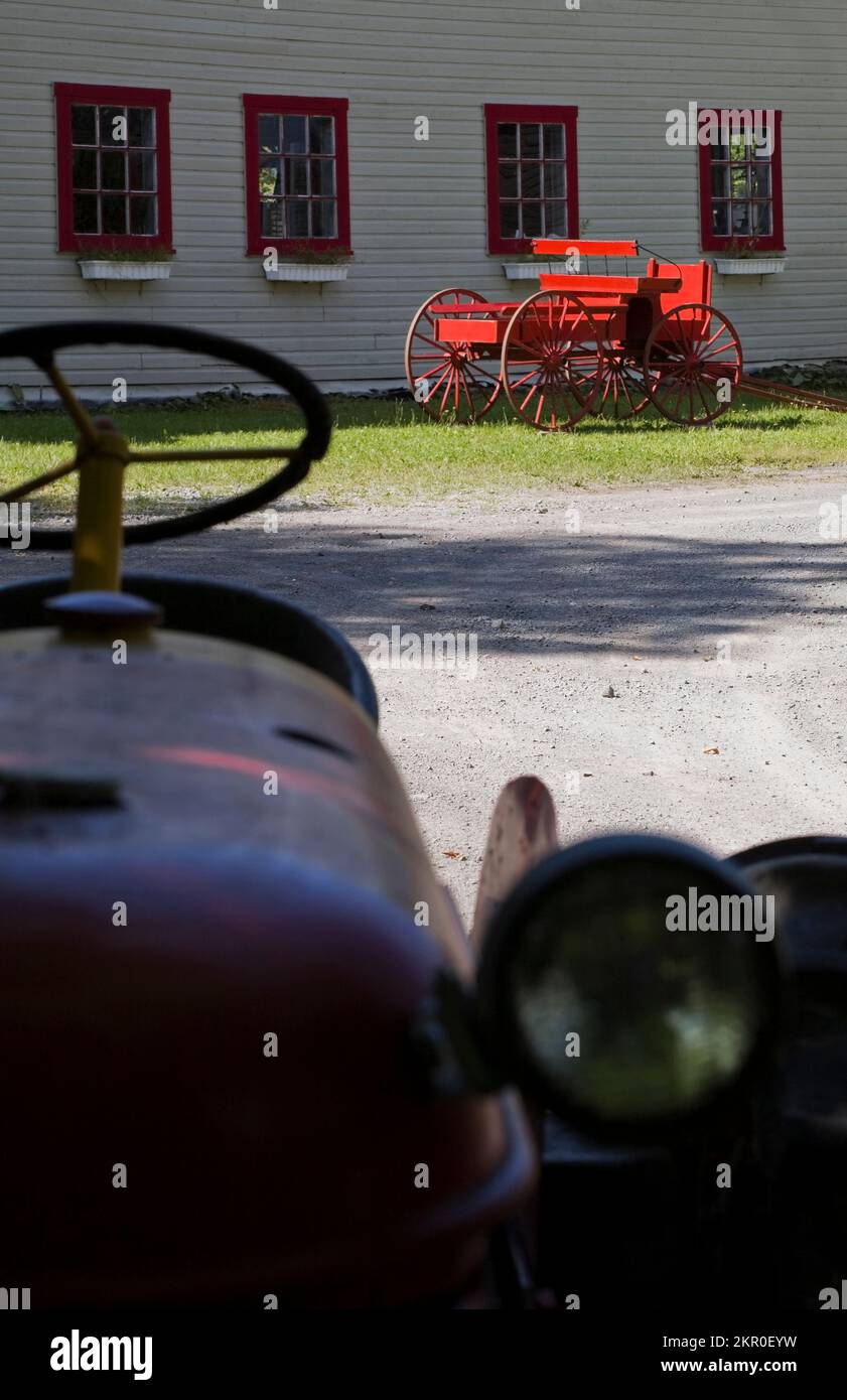 Vecchio trattore agricolo e carro antico rosso accanto al vecchio fienile bianco. Foto Stock