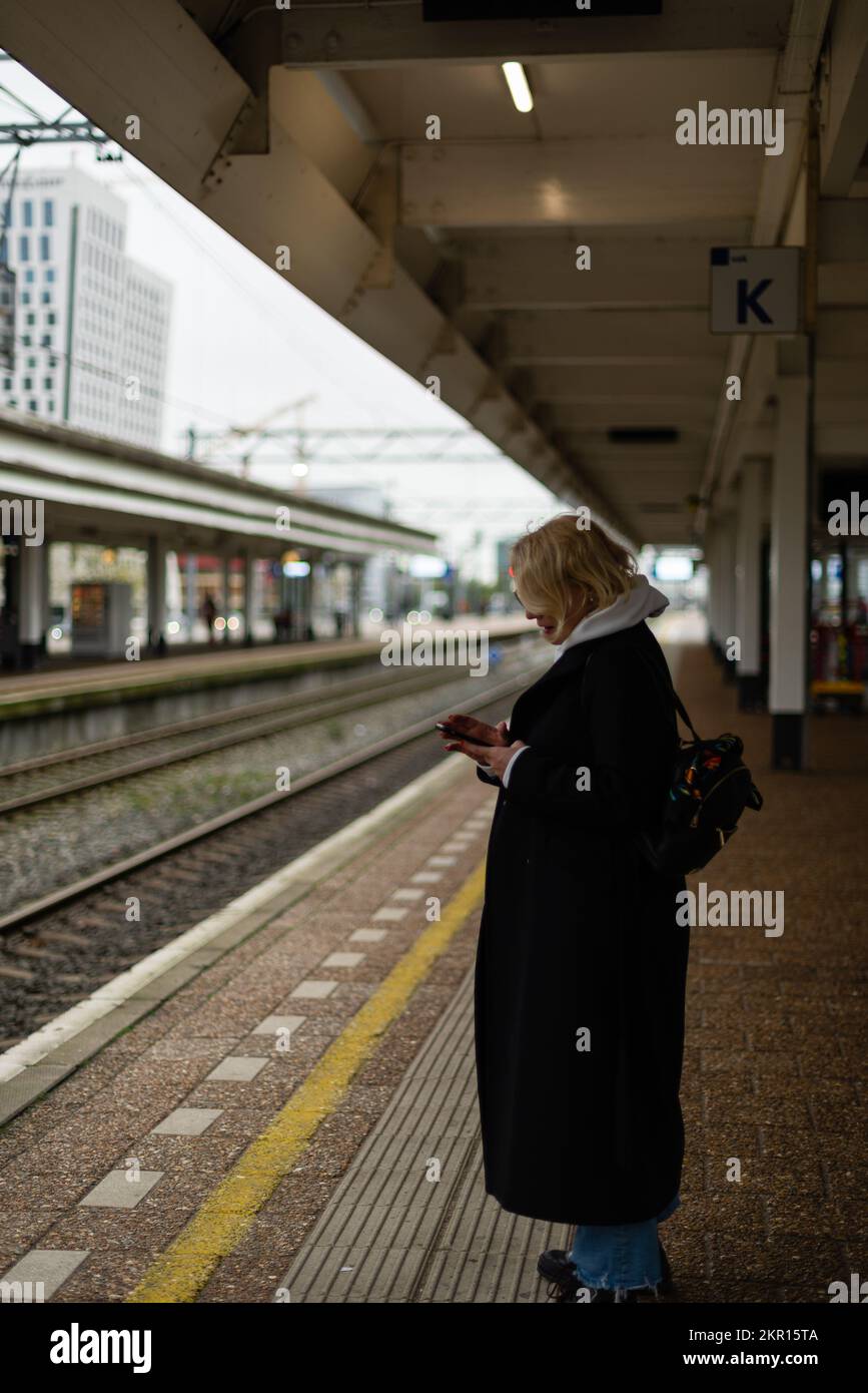 Donna sulla piattaforma della stazione di rialway che cerca con il telefono nelle mani Foto Stock