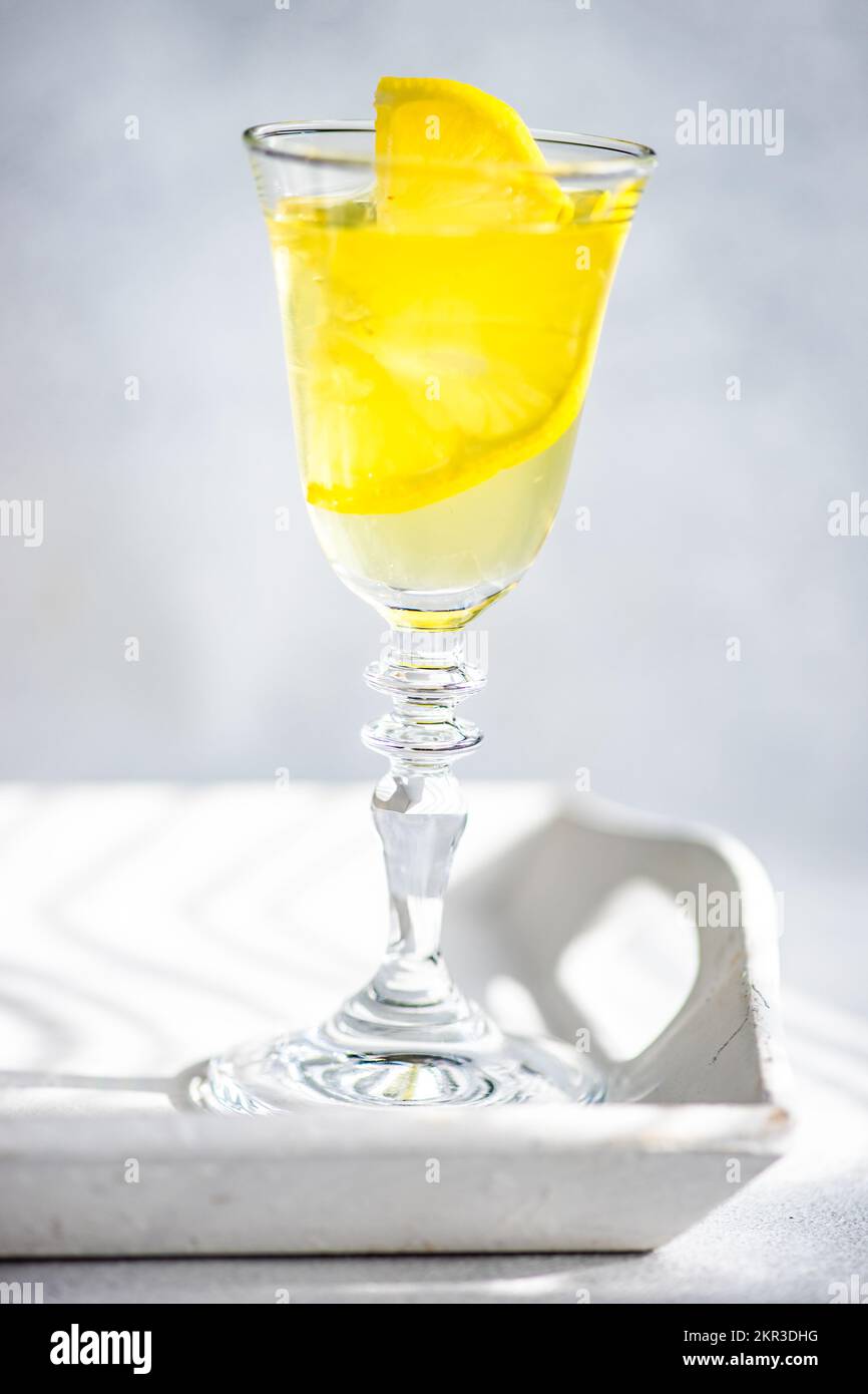 Primo piano di un bicchiere di limoncello con limone fresco su un vassoio alla luce del sole Foto Stock