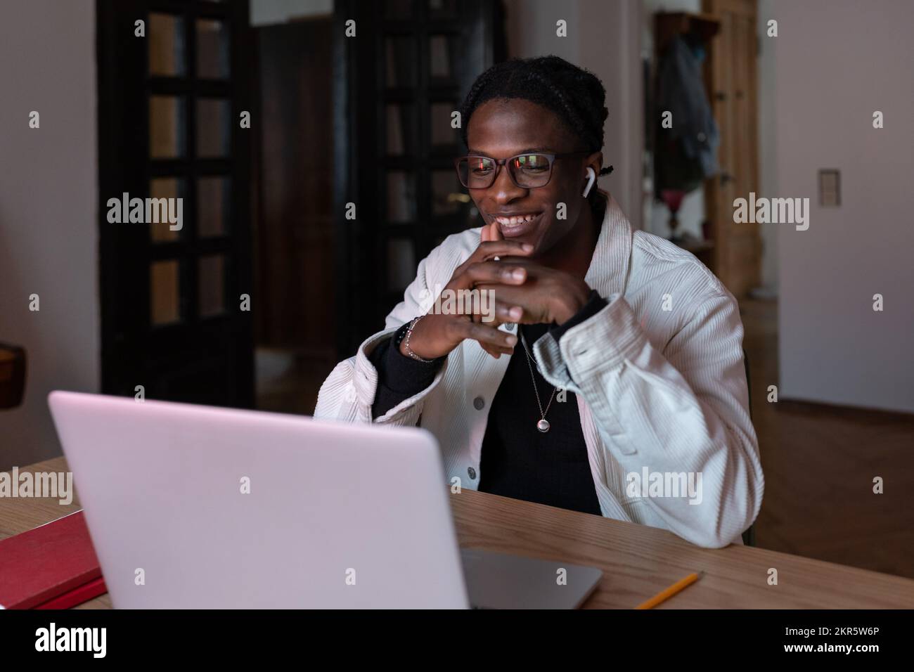 Giovane uomo africano sorridente felice lavoratore remoto in occhiali guardando lo schermo del notebook leggere e-mail Foto Stock