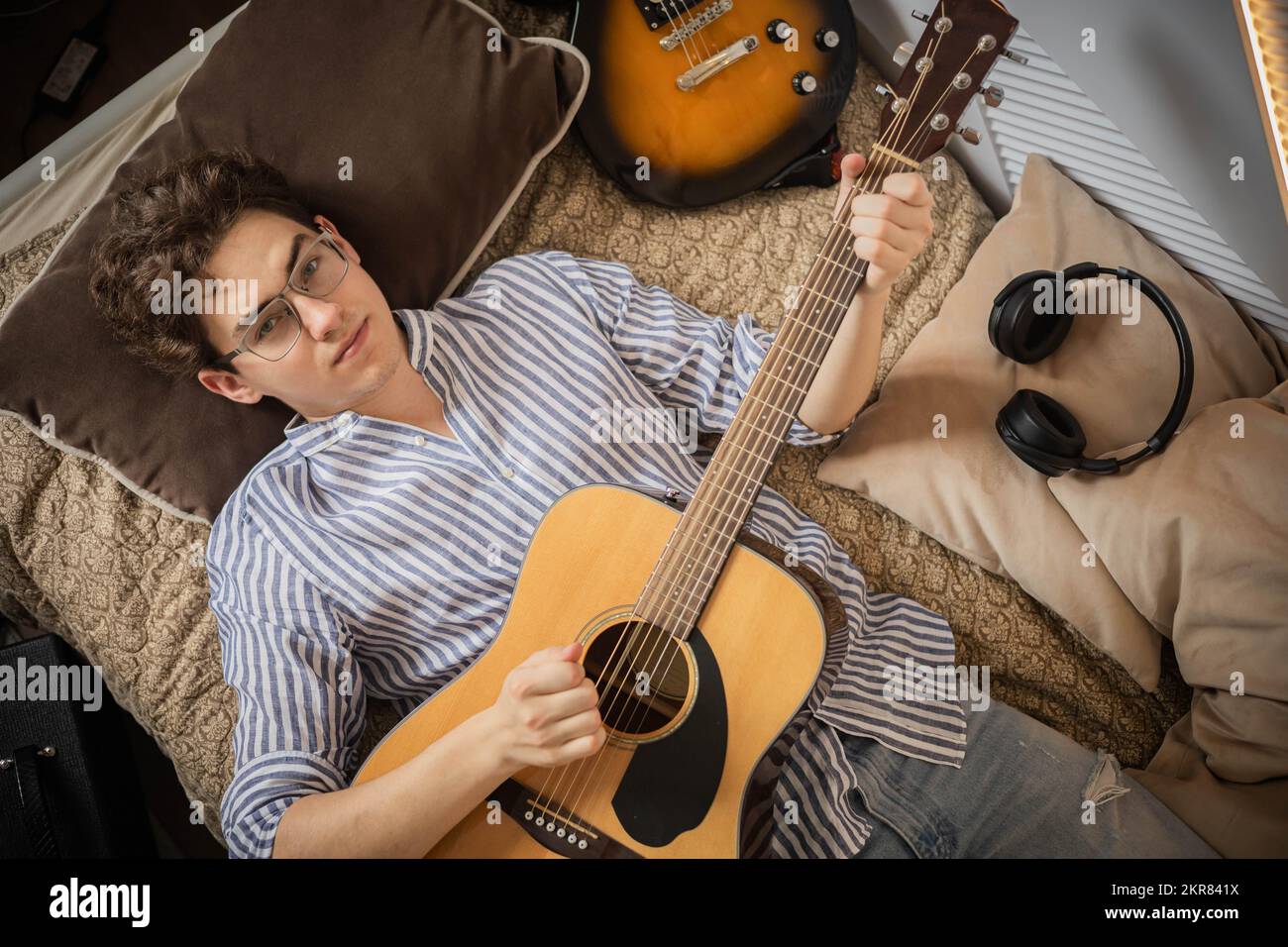 Ritratto adolescente uomo che suona chitarra acustica sdraiato su comodo  letto rilassante arte hobby intrattenimento Foto stock - Alamy