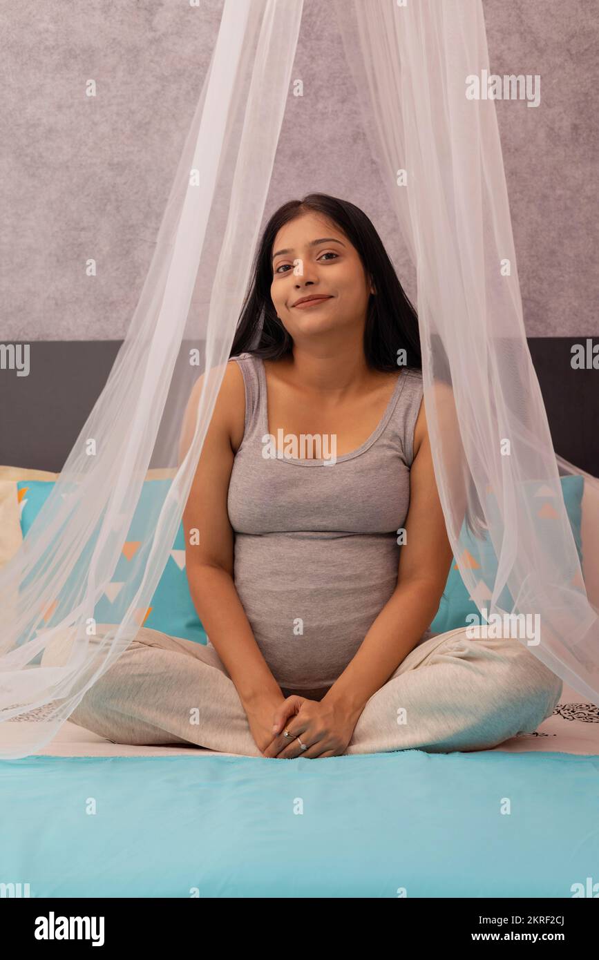 Donna incinta sorridente seduta a letto a casa Foto Stock