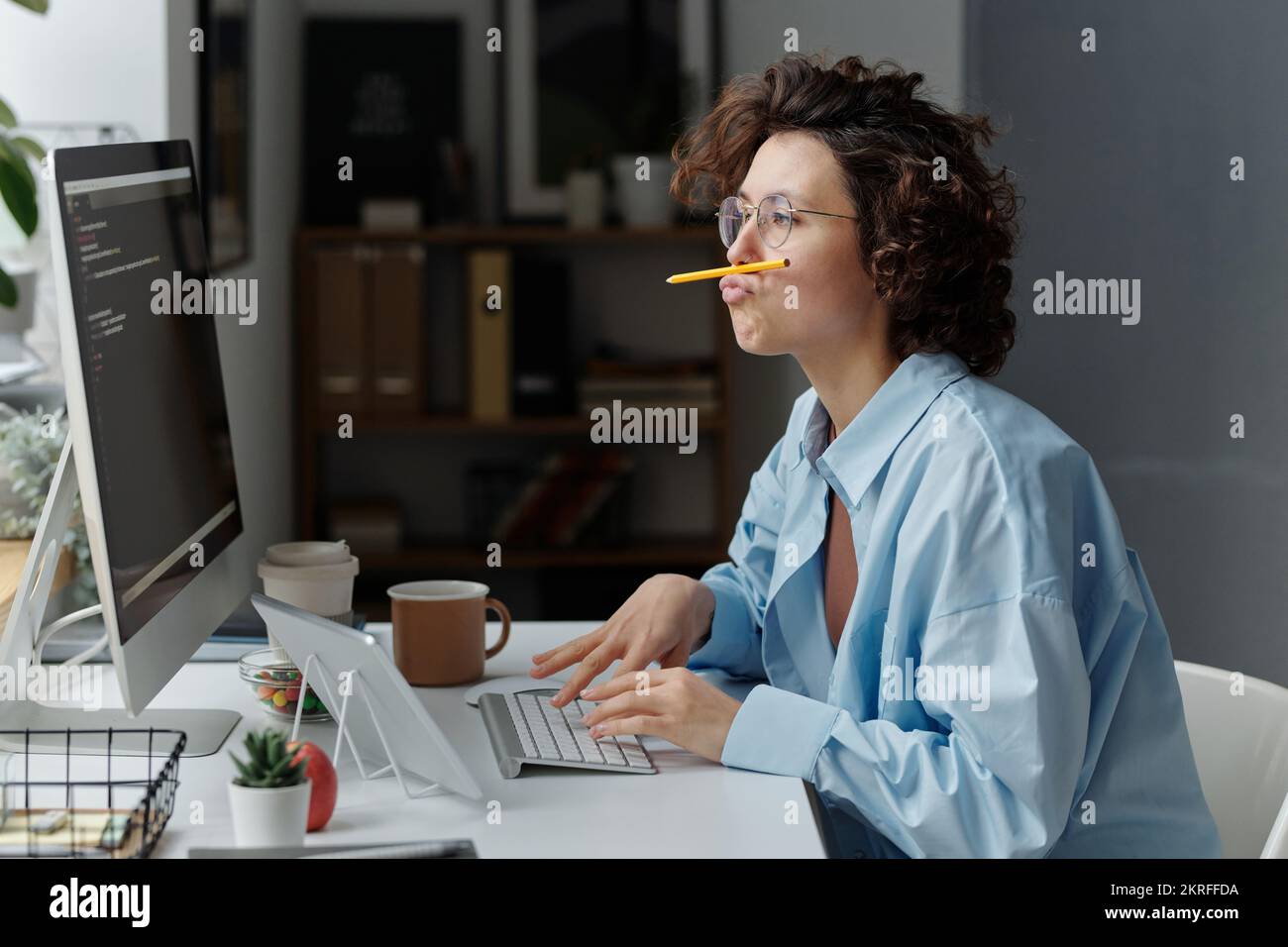 Giovane donna d'affari che imbrogliava mentre era seduto sul posto di lavoro davanti al monitor e scriveva i codici sul computer Foto Stock