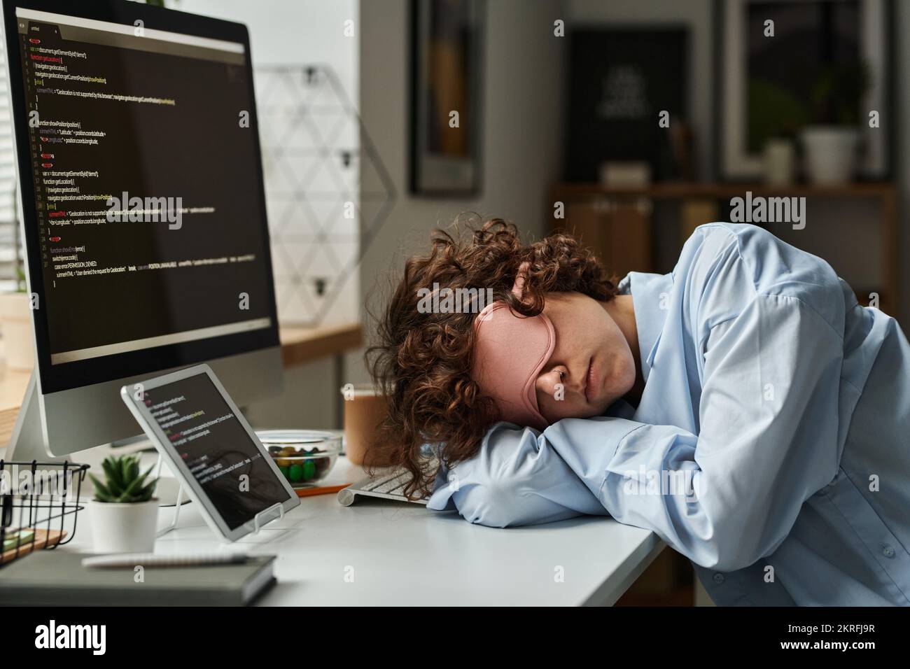 Sviluppatore IT in maschera che dorme sul suo posto di lavoro dopo un duro lavoro con il software sul computer Foto Stock