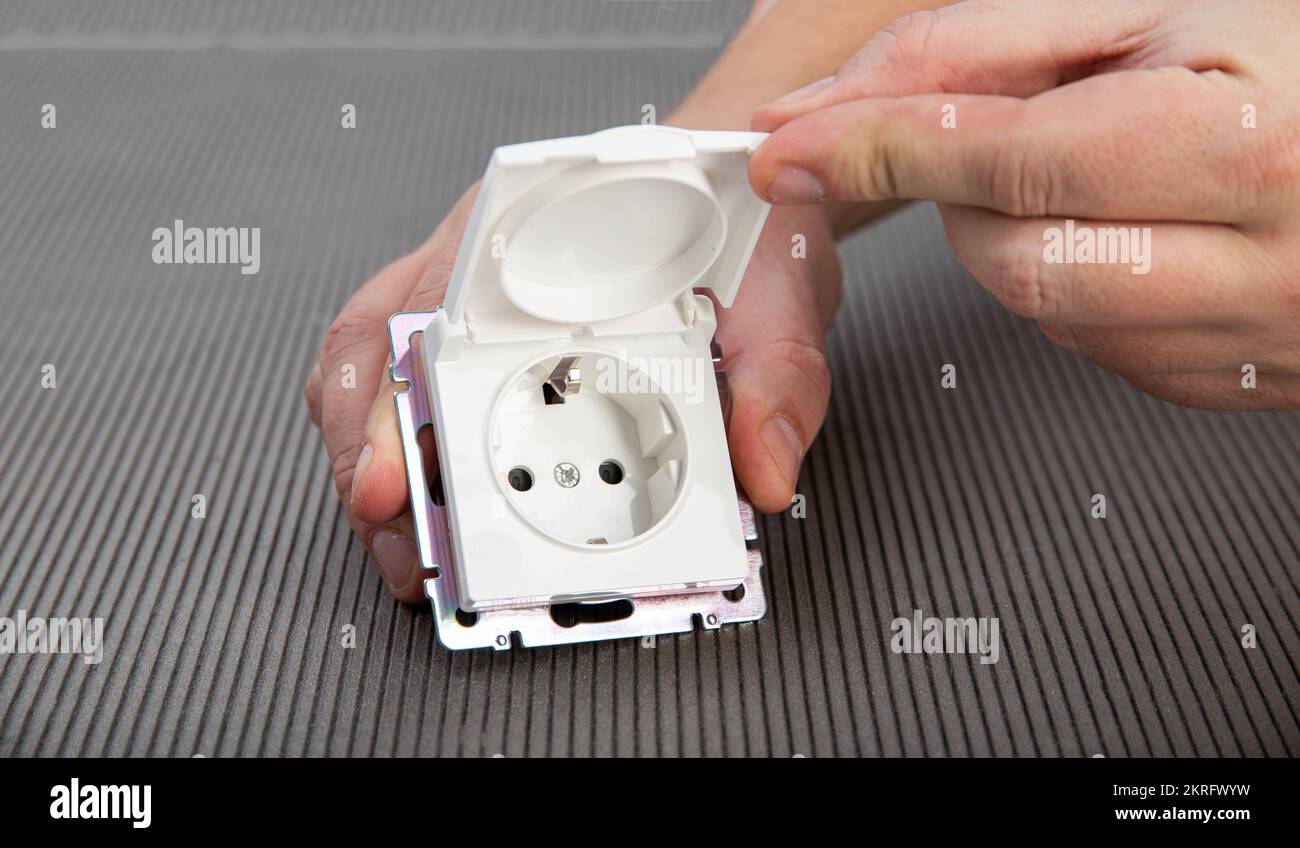 Una mano dell'uomo tiene un interruttore elettrico con una copertura protettiva su uno sfondo grigio, primo piano. Presa per esterni resistente a spruzzi e pioggia Foto Stock