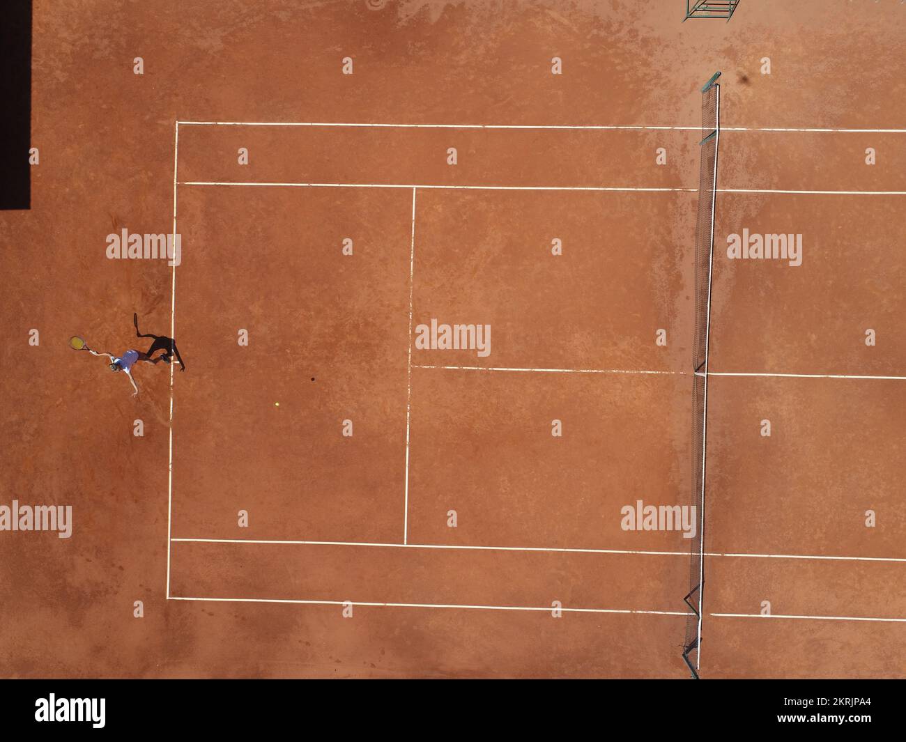 Vista aerea dall'alto di una giovane tennista femminile che gioca su un campo marrone. Ragazza professionista giocatore di tennis colpendo un backhand sul tracciato piatto del campo Foto Stock