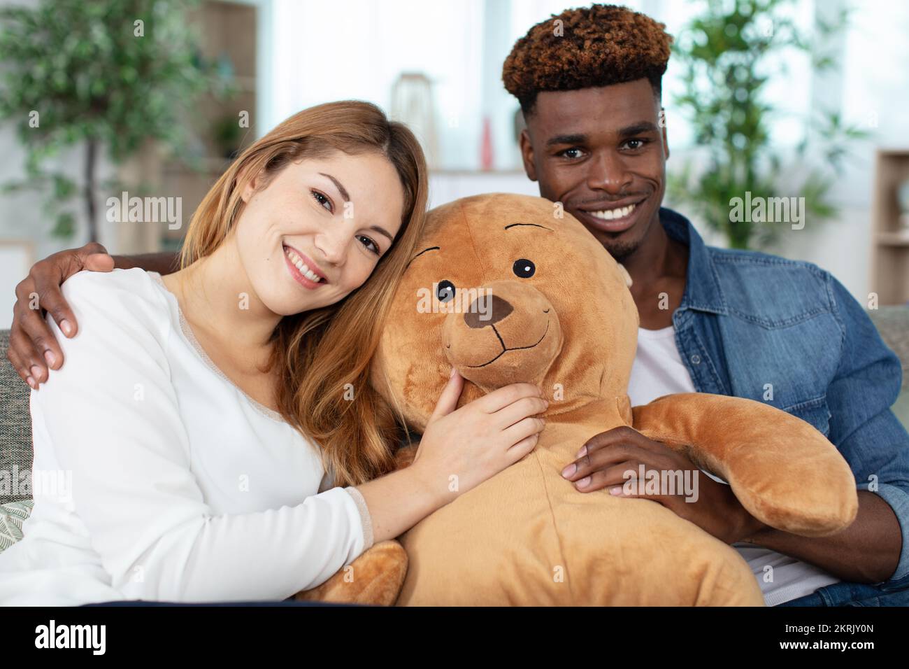 coppia sedette sul divano con un grande orsetto di peluche Foto Stock