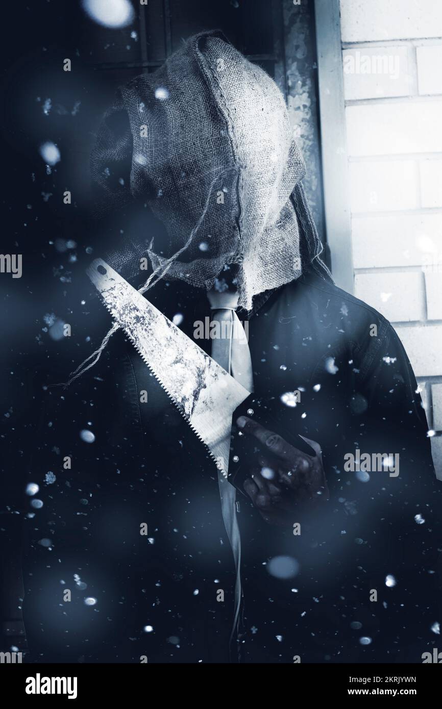 Foto blu freddo di un assassino mascherato in piedi sotto la neve cadente con un'arma omicida. Uccisione a sangue freddo Foto Stock