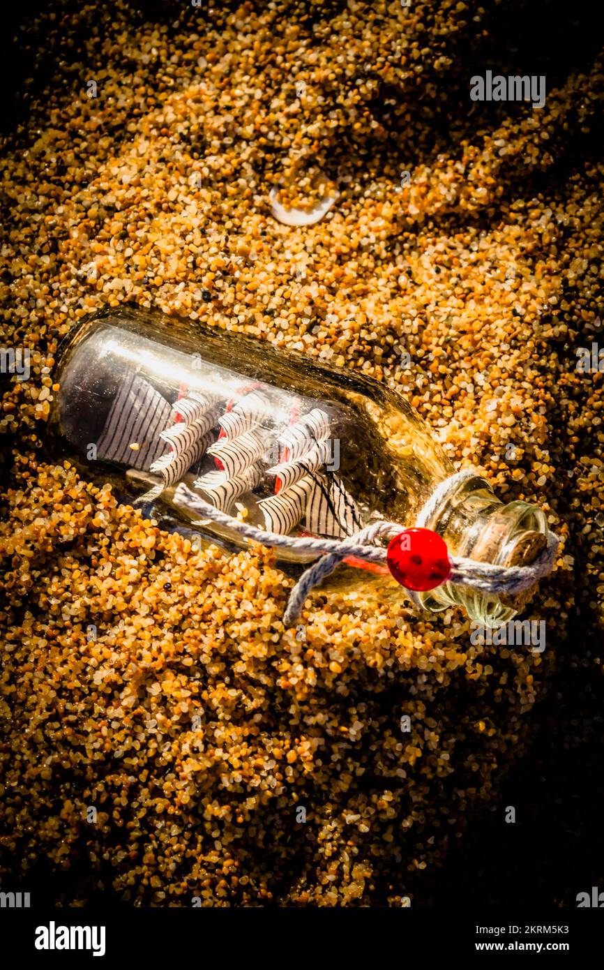 Primo piano della nave in bottiglia di vetro su sabbia marrone. Barche in bottiglia di sabbia bianca Foto Stock