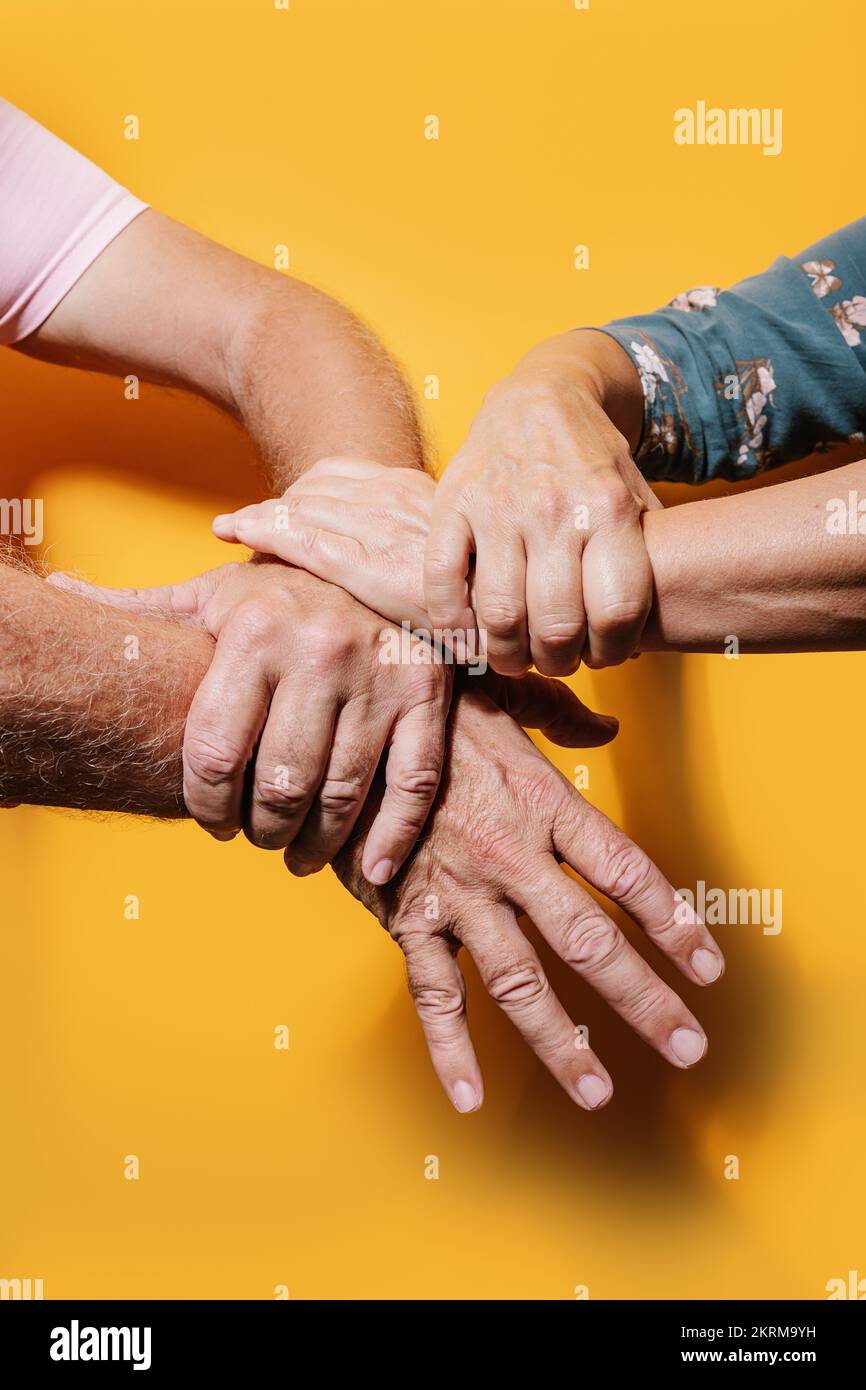 Ritaglia persone anonime anziane che si toccano le mani su sfondo giallo Foto Stock