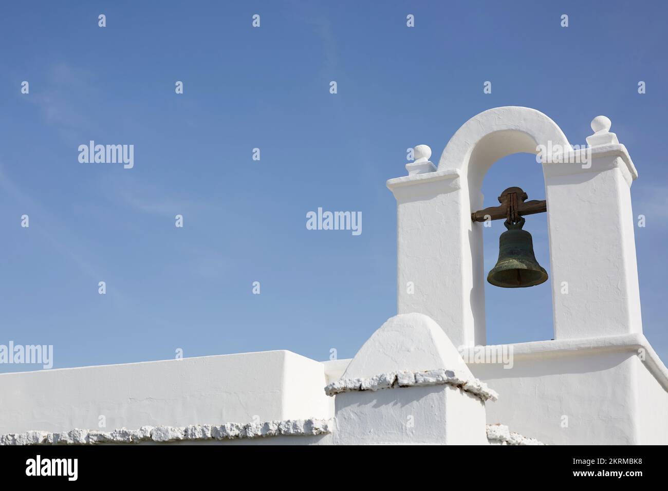 Basso angolo di facciata di vecchio edificio in pietra bianca con campana di metallo in torre ad arco sotto cielo blu senza nuvole Foto Stock
