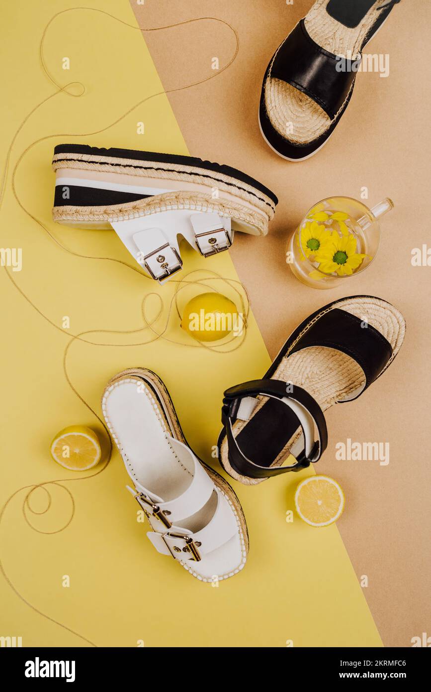 Vista dall'alto composizione di vari sandali con plateau in vimini disposti su sfondo multicolore con bicchiere di limonata e limoni freschi maturi Foto Stock