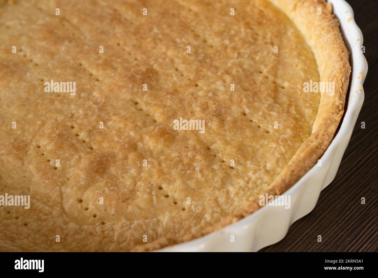Una sfoglia di pasta frolla cotta cieca in una teglia/quiche di ceramica bianca, pronta per il ripieno. Concetto - preparazione alimentare Foto Stock
