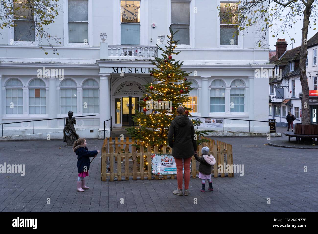 Una madre e le sue due figlie che guardano un albero di Natale decorato e illuminato in Market Place, Basingstoke in cima alla città. Dicembre 2022 Foto Stock