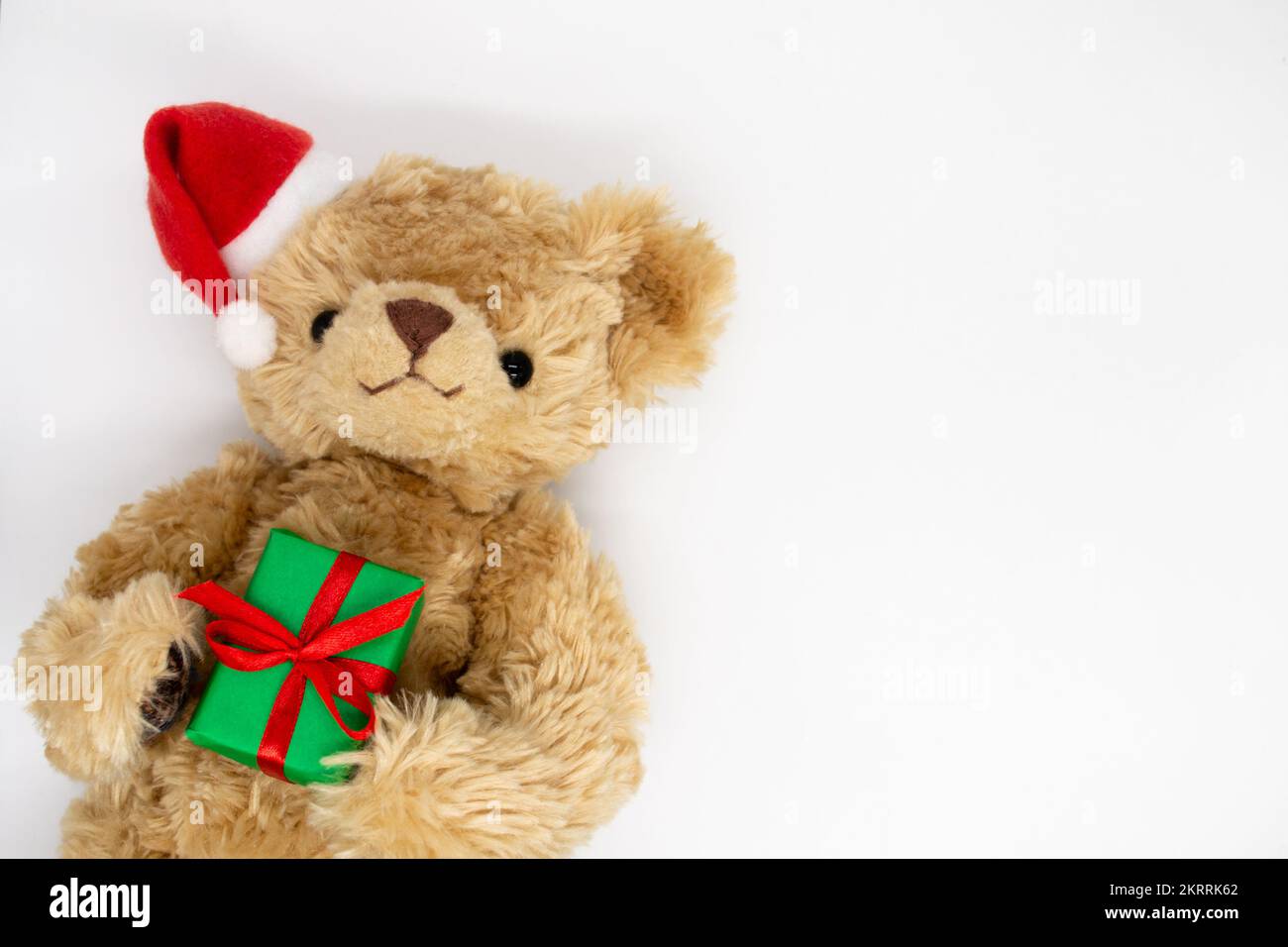 Un orsacchiotto peluche giocattolo in un cappello rosso di Babbo Natale con un pompom su un orecchio, tenendo le scatole regalo verdi nelle sue zampe. Sfondo bianco, spazio di copia. Il co Foto Stock