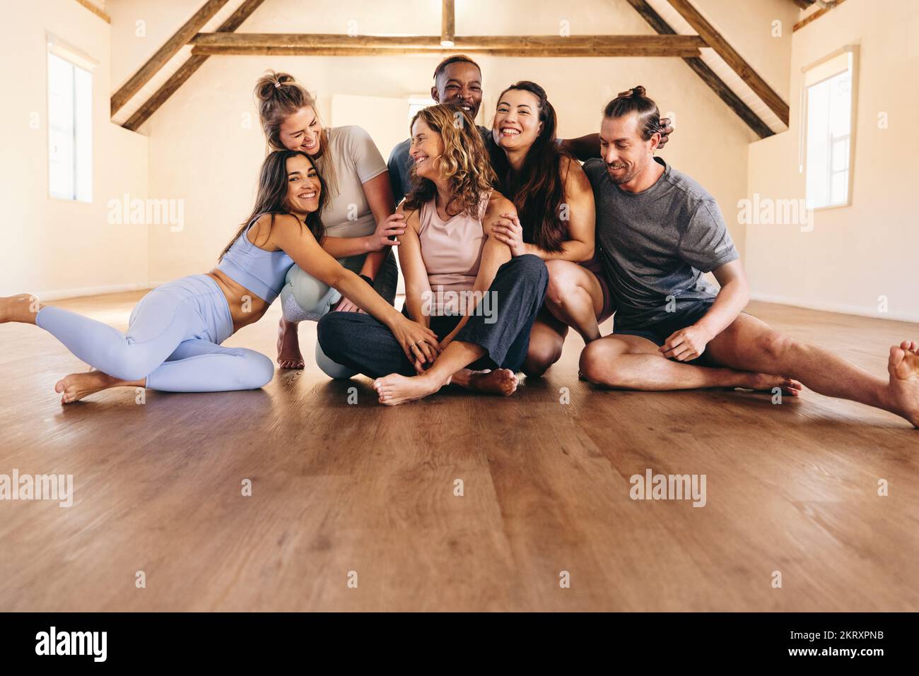 Le persone ridono insieme mentre si siedono sul pavimento in uno studio di yoga. Amici felici di fitness che prendono una pausa da una sessione di yoga. Gruppo di diversi peopl Foto Stock