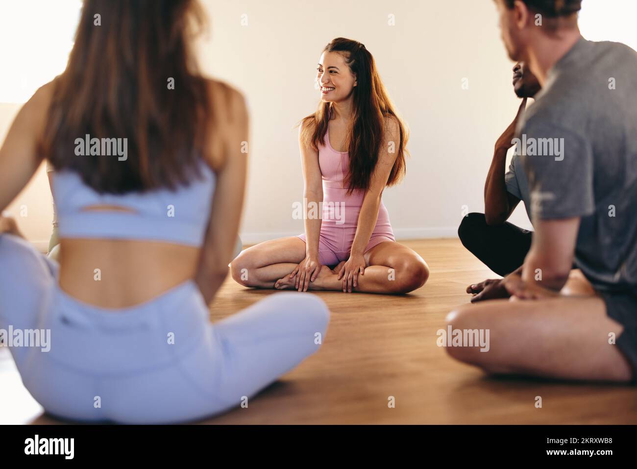 Gruppo di persone felici che comunicano tra loro mentre si siedono in cerchio. persone in forma fisica che condividono consigli di coping in un gruppo di supporto yoga. Giovani persone Foto Stock
