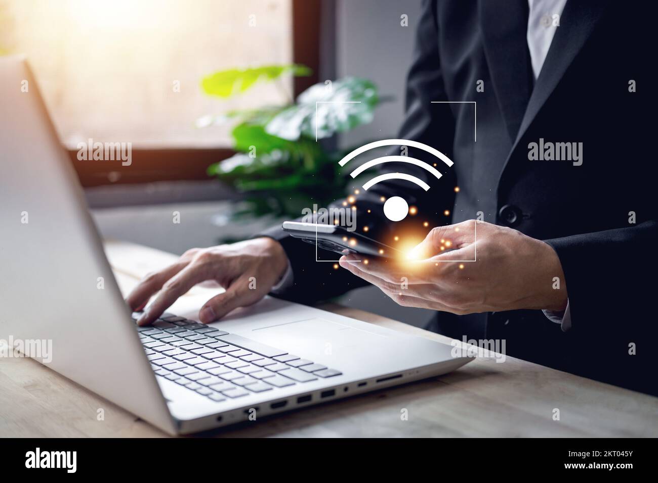 Uomo d'affari utilizza lo smartphone con il simbolo wifi e il notebook per la digitazione delle mani (laptop). La tecnologia aziendale collega il concetto digitale. Foto Stock