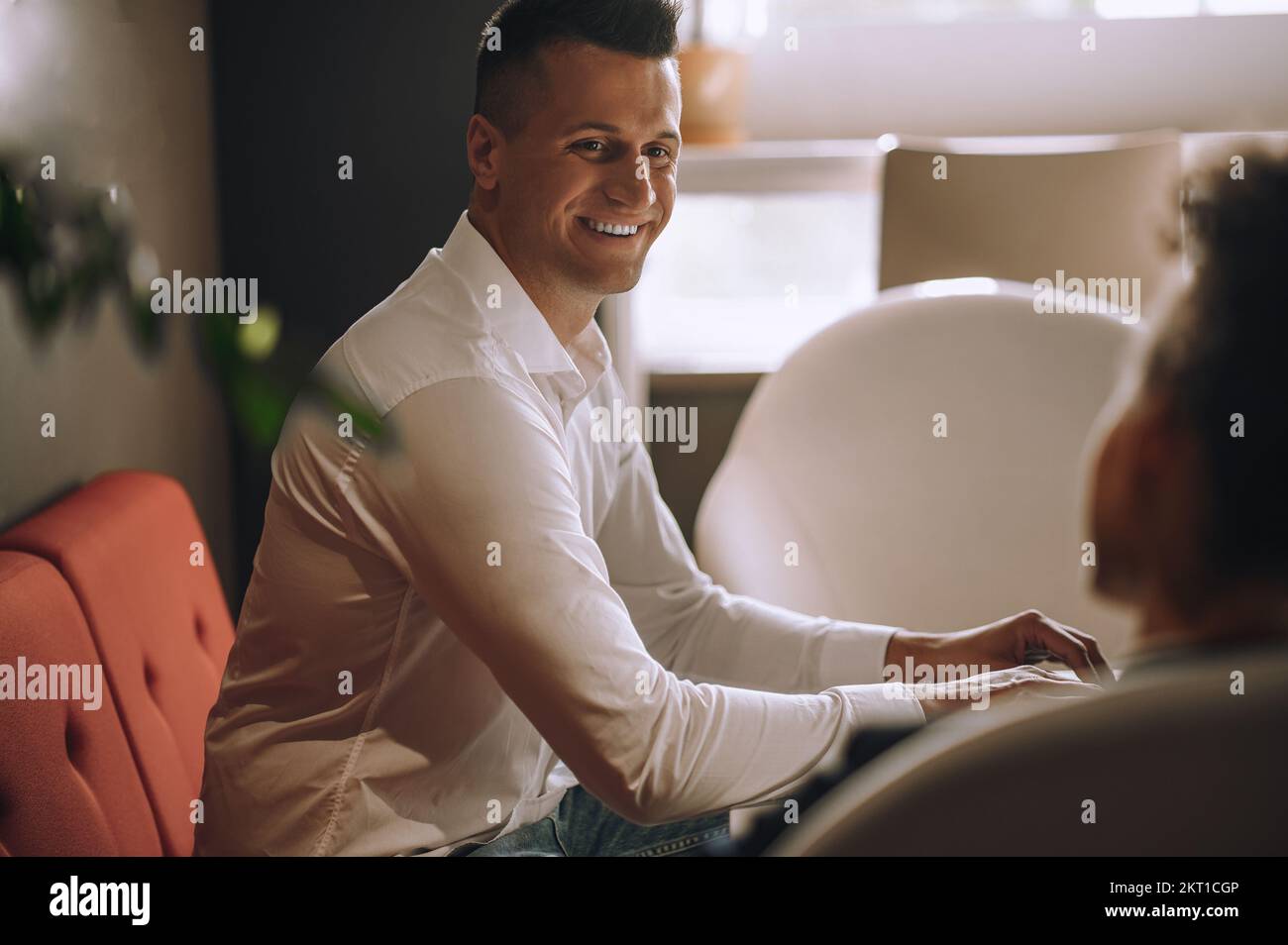 Un uomo sorridente che guarda un collega seduto in ufficio Foto Stock