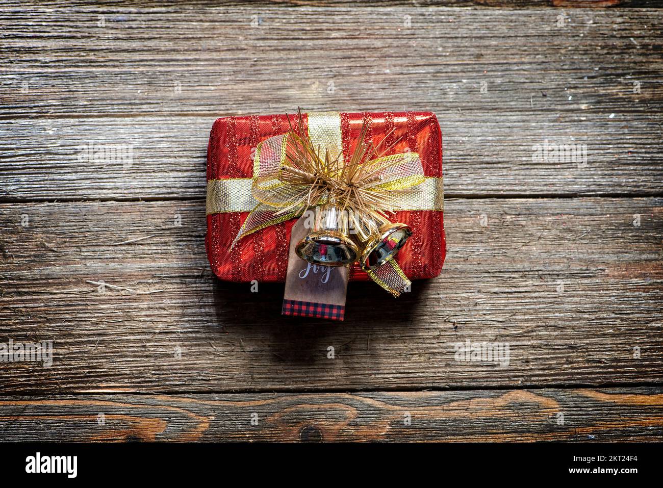 Piccola scatola regalo rossa e dorata su uno sfondo rustico in legno, in stile casale. Foto Stock