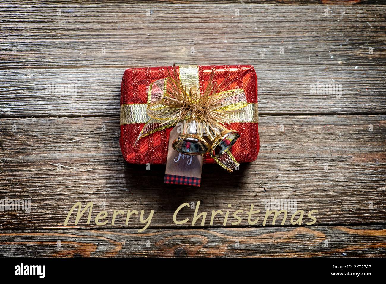 Piccola scatola regalo rossa e d'oro su uno sfondo rustico in legno, stile casale, buon testo di Natale. Foto Stock