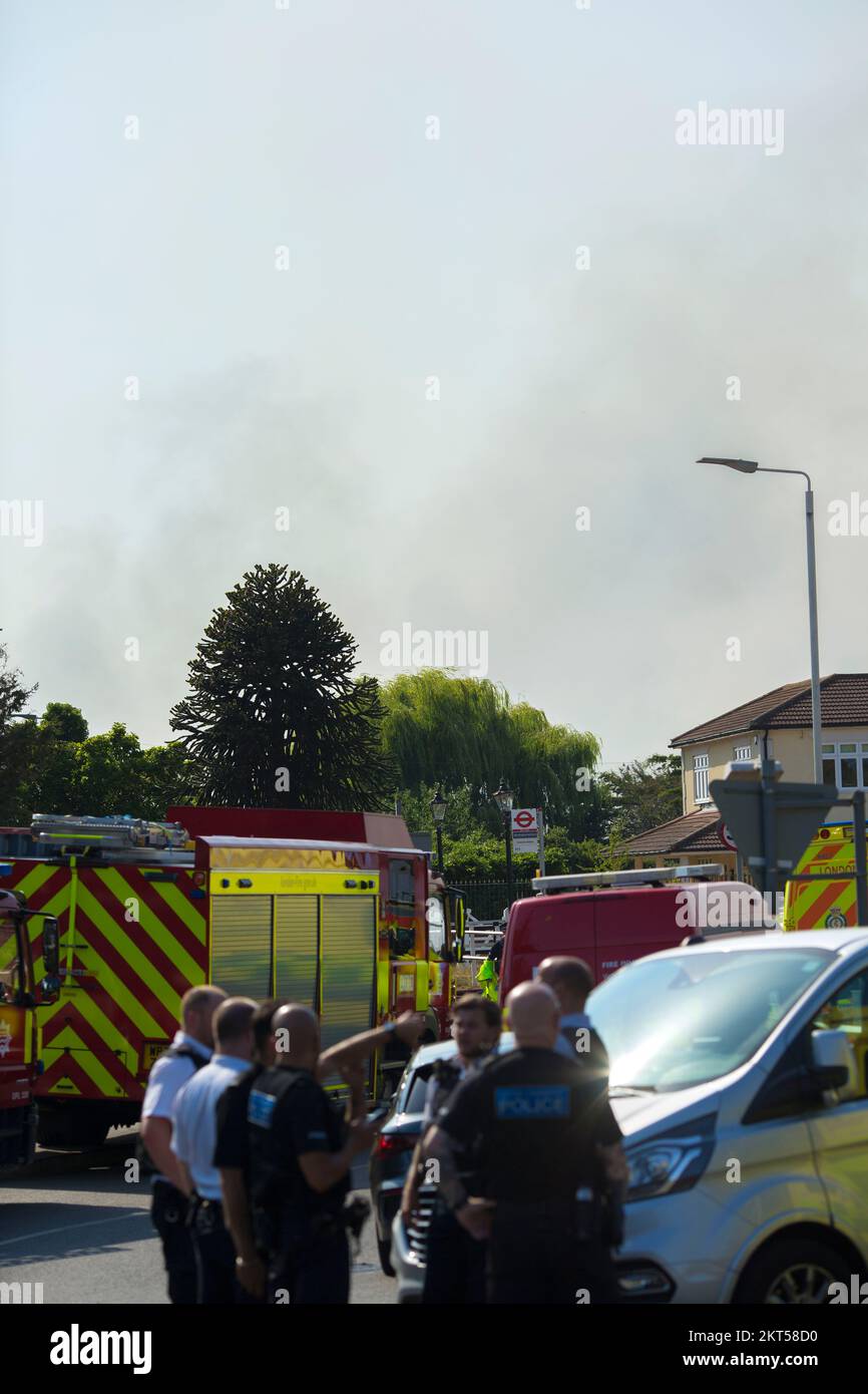 Il fumo proveniente da un incendio si vede dietro gli agenti di polizia a Wennington, nella parte orientale di Londra, poiché il Regno Unito ha registrato temperature superiori a 40 gradi. Foto Stock