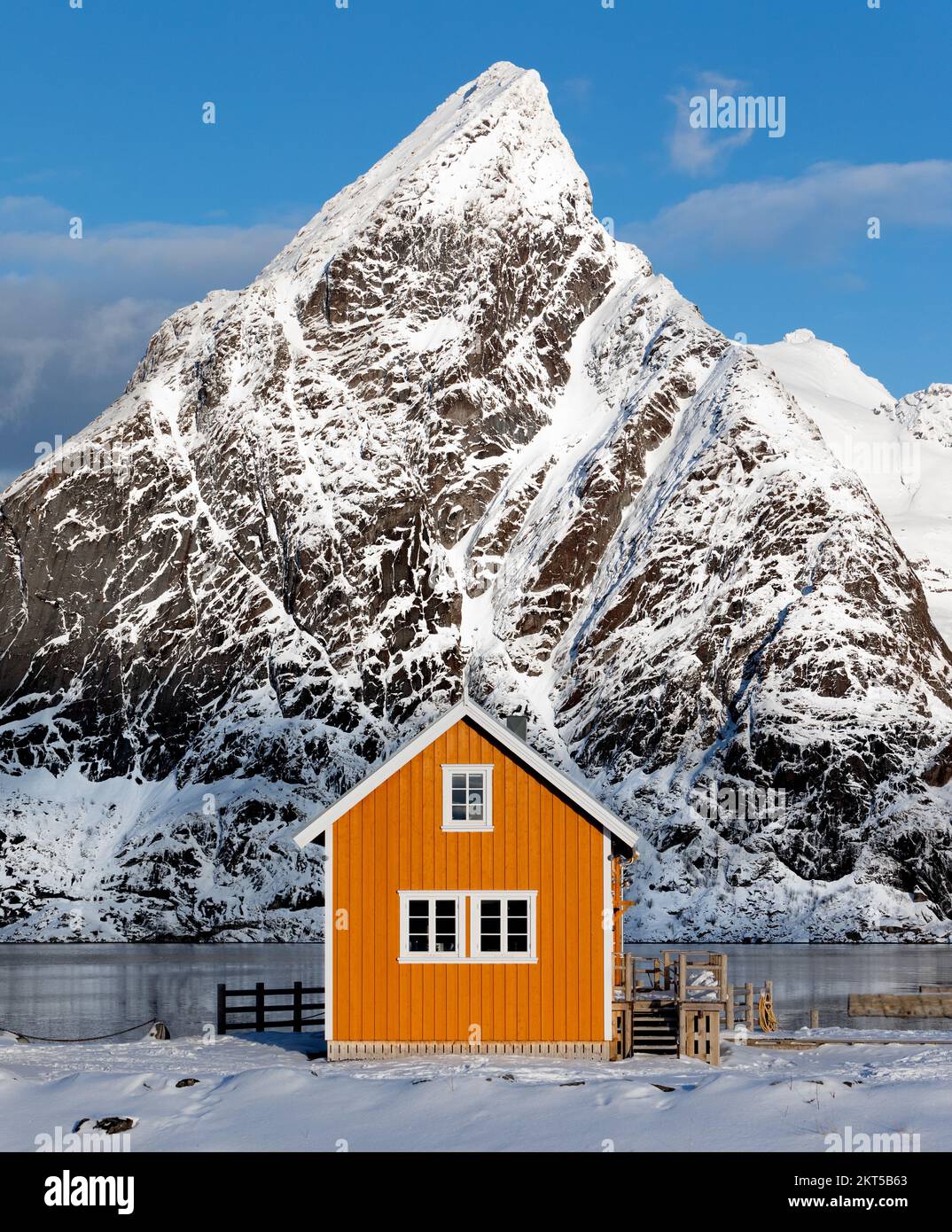 Una tradizionale cabina gialla di Rorbu con la cima del Monte Olstinden posta come sfondo drammatico nel villaggio di Sakrisoya, arcipelago delle Isole Lofoten, Norw Foto Stock