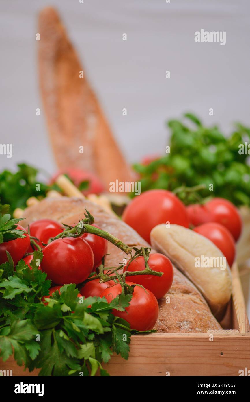 Pomodori rossi freschi bio maturi con pane bianco, prezzemolo e foglie di basilico in una scatola di legno in un mercato di Street food, in primo piano, verticale Foto Stock