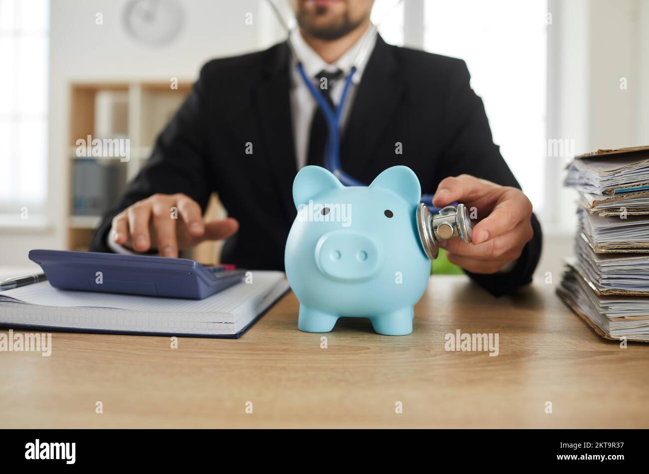 Consulente finanziario maschile o contabile ispeziona e ascolta la piggy bank con stetoscopio. Foto Stock
