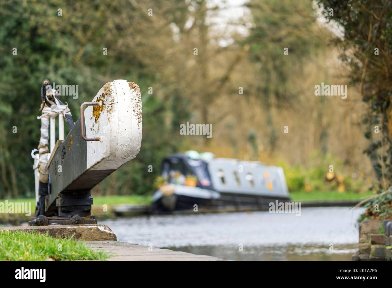 Primo piano ad angolo basso di un cancello di blocco in uso su un canale del Worcestershire, Regno Unito, con una barca stretta isolata / barca del canale ormeggiata sullo sfondo. Foto Stock
