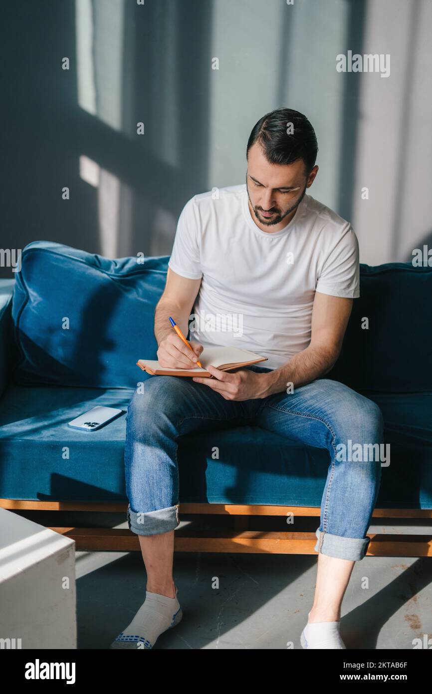 L'uomo seduto sul divano che scrive i pensieri in giornale. Concetto aziendale. Concetto pensivo. Foto Stock