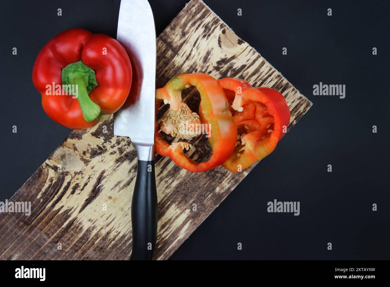 Pepe di capra e coltello da cucina disposti sul tagliere su sfondo scuro. Cucina, cibo e concetto di casa - primo piano di taglio del pepe sul tagliere Foto Stock