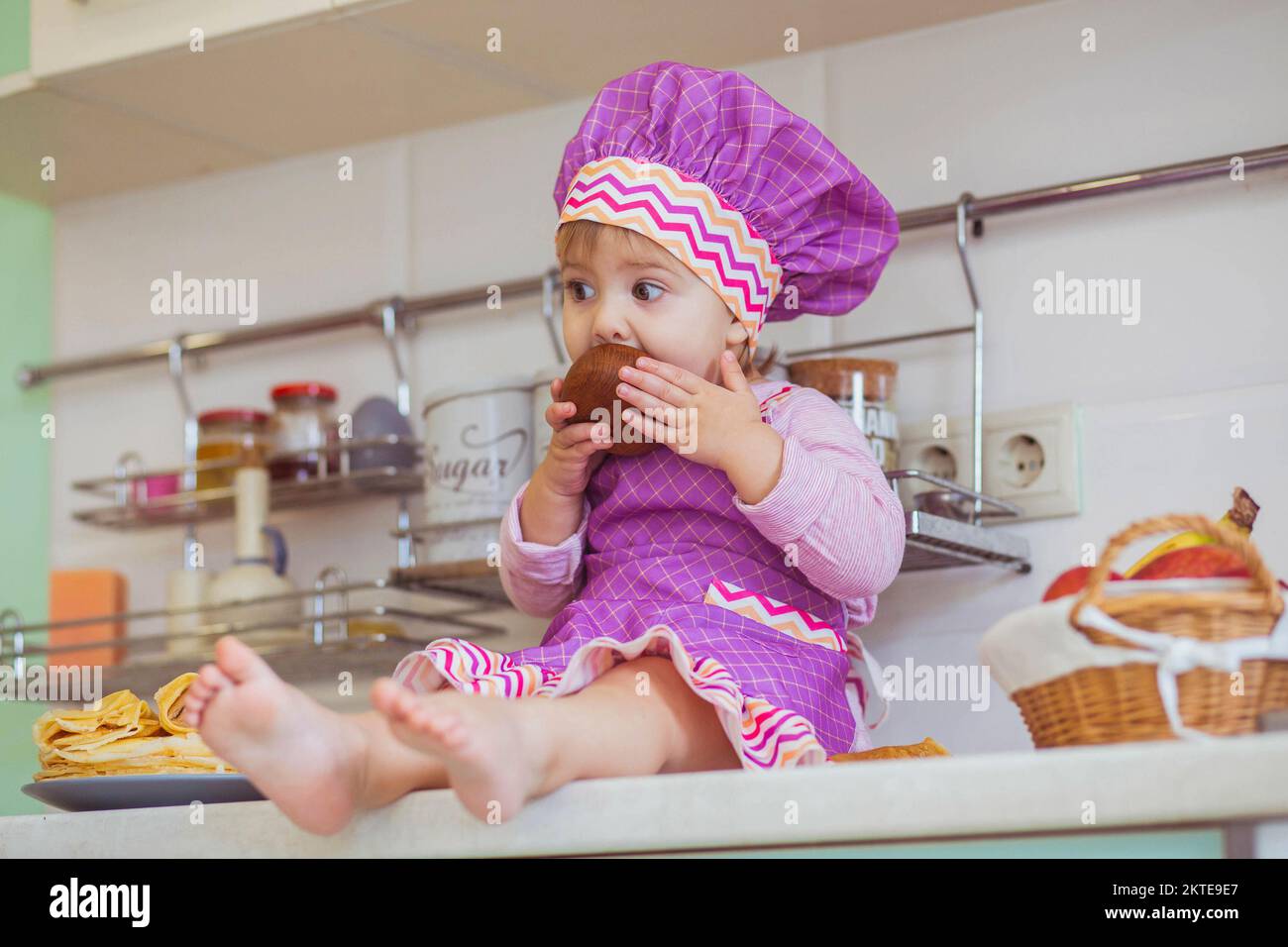 bellissimo bambino in un grembiule mangiare miele sul tavolo da cucina Foto Stock