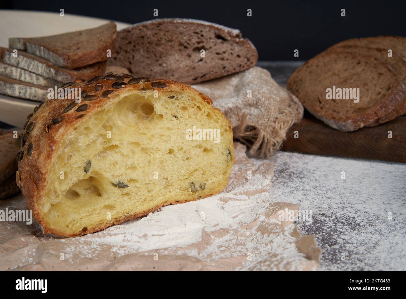 Diversi tipi di pane affettato e una pagnotta su uno sfondo di legno. Farina versata. Vista frontale. Spazio di copia. Una pagnotta tagliata a metà. Pane fresco e croccante. Foto Stock