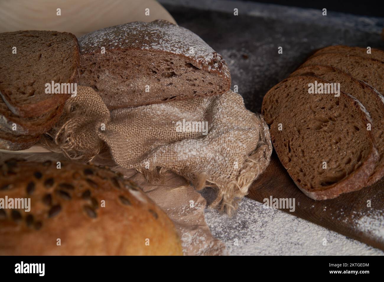 Vista dall'alto di vari tipi di pane, affettato e intero, farina, carta stropicciata e tela di tela su un tavolo di legno. Angolo alto. Foto Stock