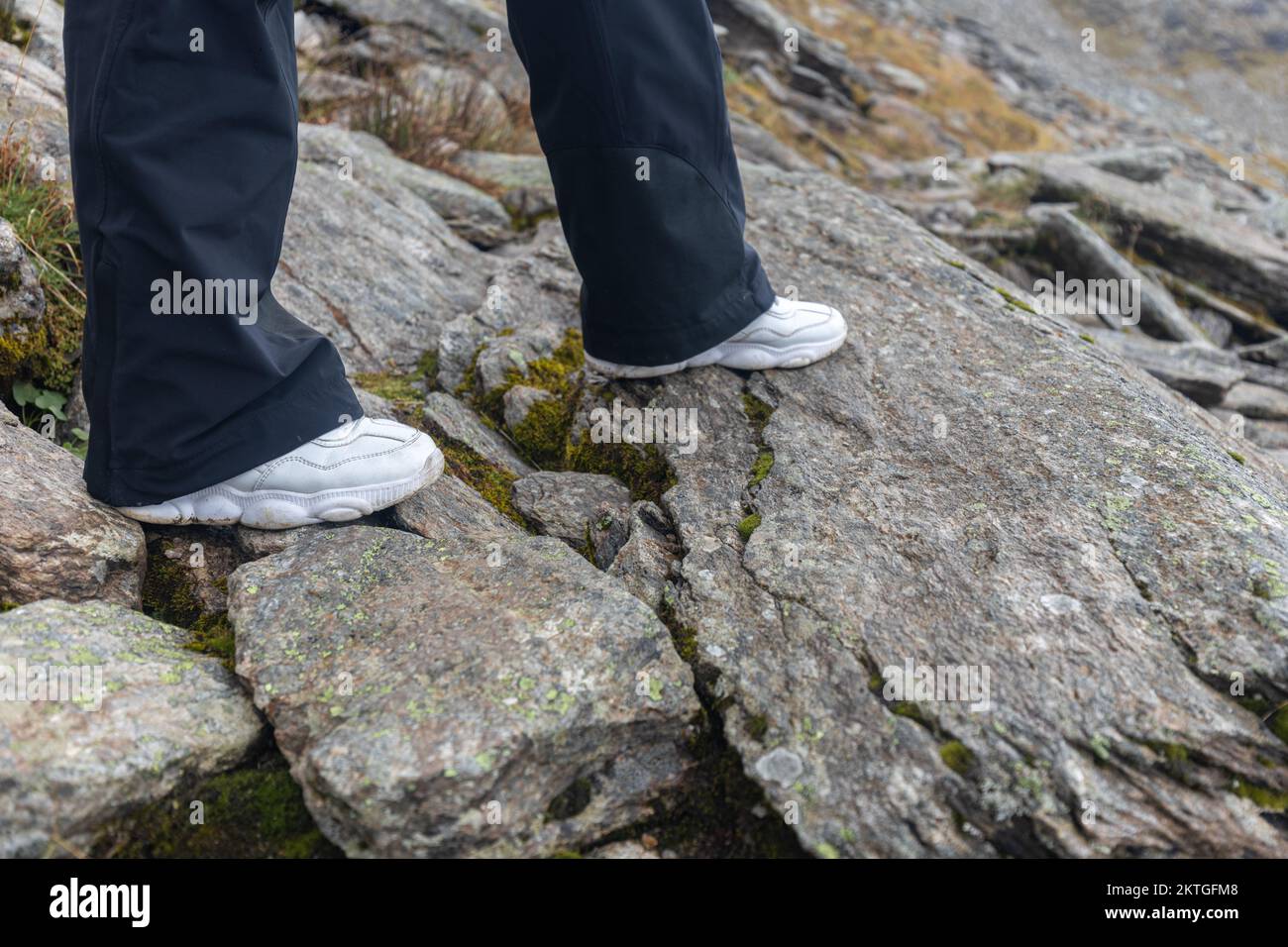 Le gambe di una donna in sneakers bianche passano attraverso un sentiero roccioso di montagna, le alpi austriache. Foto di alta qualità Foto Stock