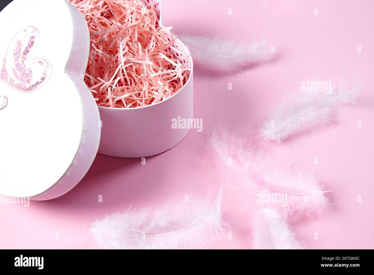 Scatola regalo a forma di cuore su sfondo rosa con piume . Layout per il prodotto.angolo alto. Vacanze, romanticismo, San Valentino, prodotti cosmetici, profumo, Foto Stock