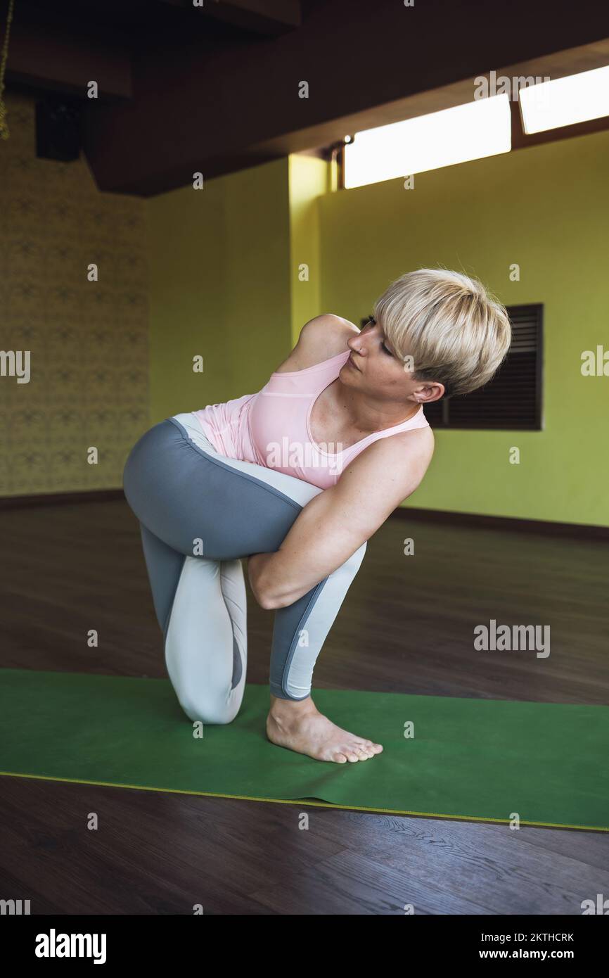 Una donna che conduce uno stile di vita sano e pratica yoga esegue un esercizio di vatajanasana, posa di cavalli, allenamenti su un tappetino in studio Foto Stock