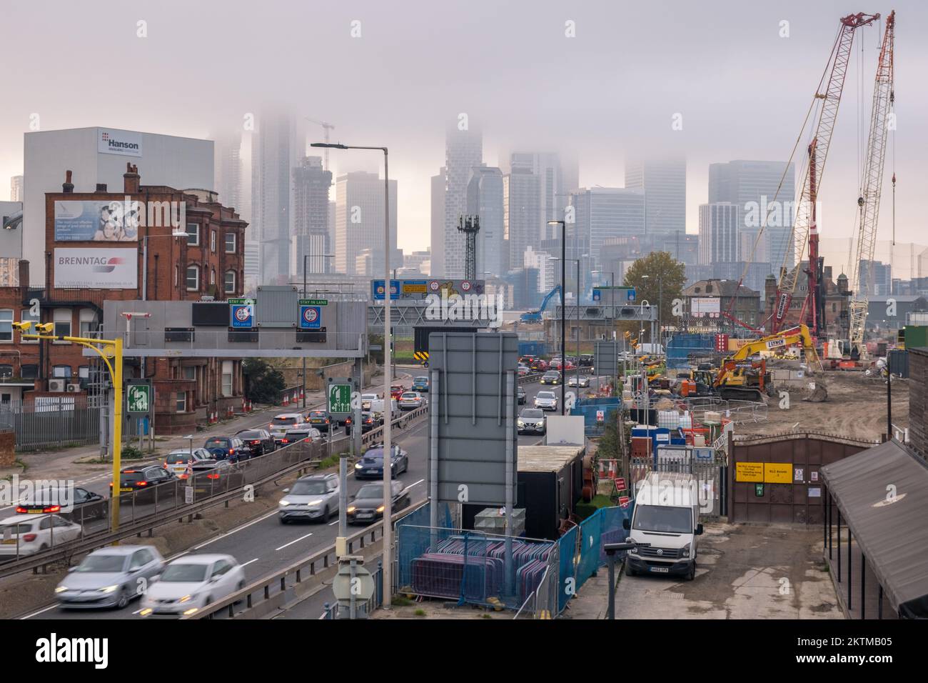 Nebbia, skyline dell'Isola di Dogs in lontananza, punto di vista dalla strada di avvicinamento Sud del Tunnel Blackwall, con traffico intenso, Greenwich, Londra Sud. Foto Stock