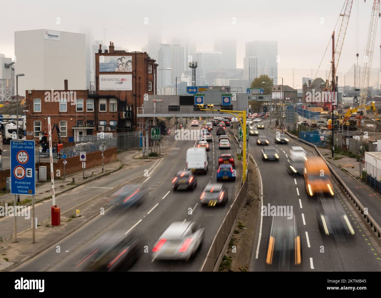 Nebbia, skyline dell'Isola di Dogs in lontananza, punto di vista dalla strada di avvicinamento Sud del Tunnel Blackwall, con traffico intenso, Greenwich, Londra Sud. Foto Stock