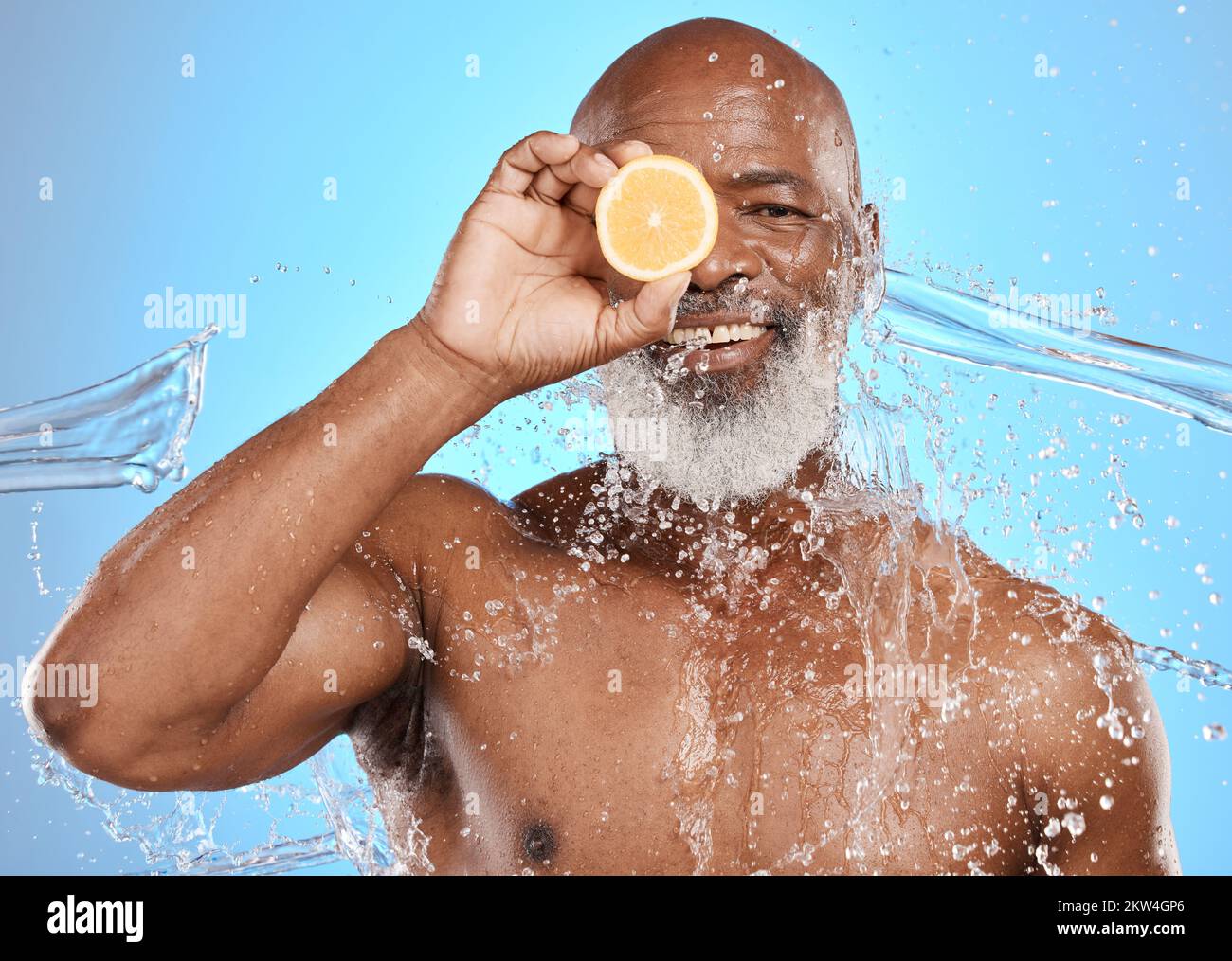 Uomo viso, frutta o acqua spruzzi su sfondo blu in studio per il trattamento della vitamina C, salute sanitaria o igiene di pulizia. Ritratto, sorriso felice Foto Stock