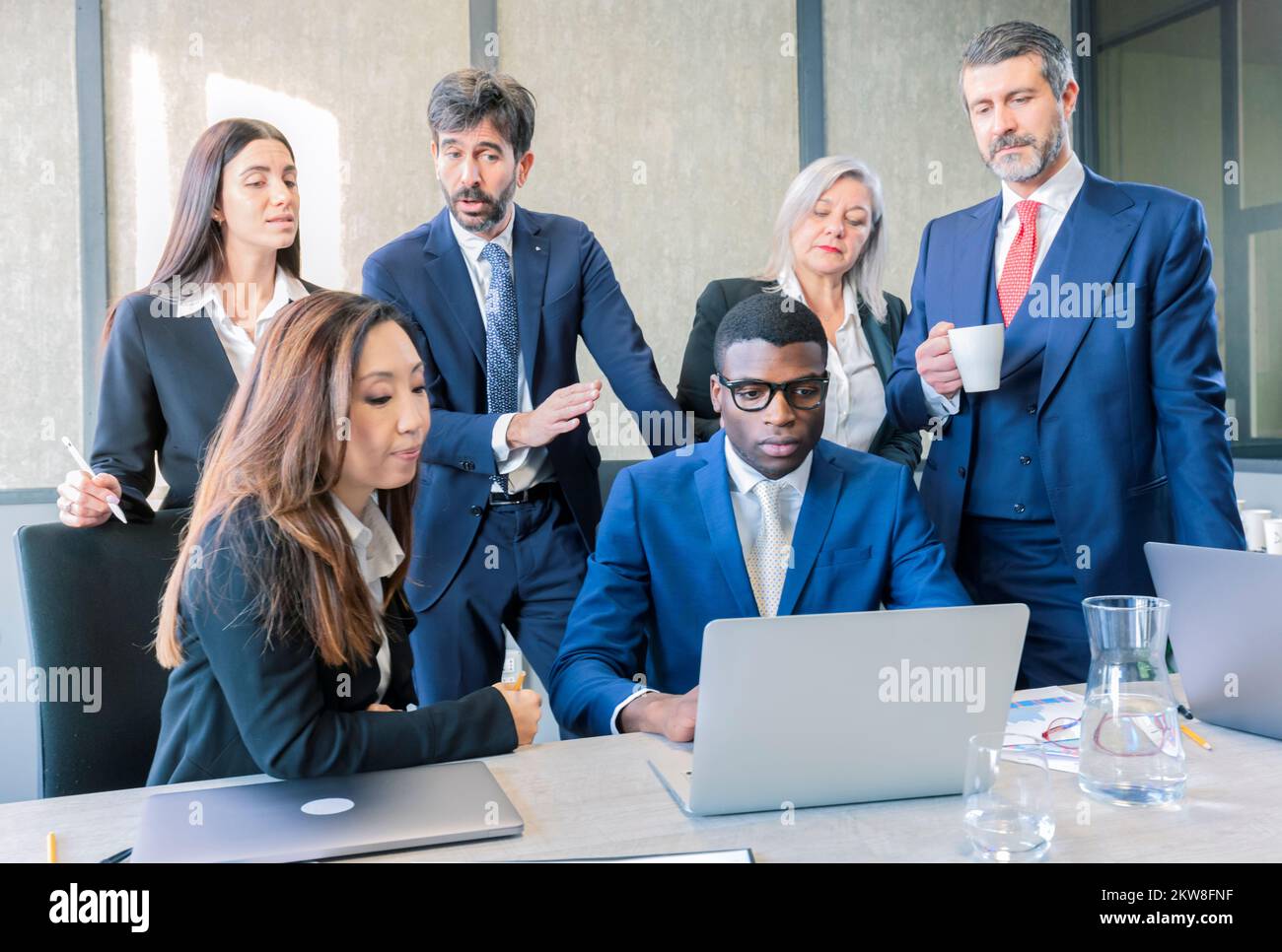 Gruppo di colleghi diversi in formale vestire tavola circondata con computer portatile, take-away caffè e fogli di carta e cartelle, lavorando in uno spazio aperto di Foto Stock