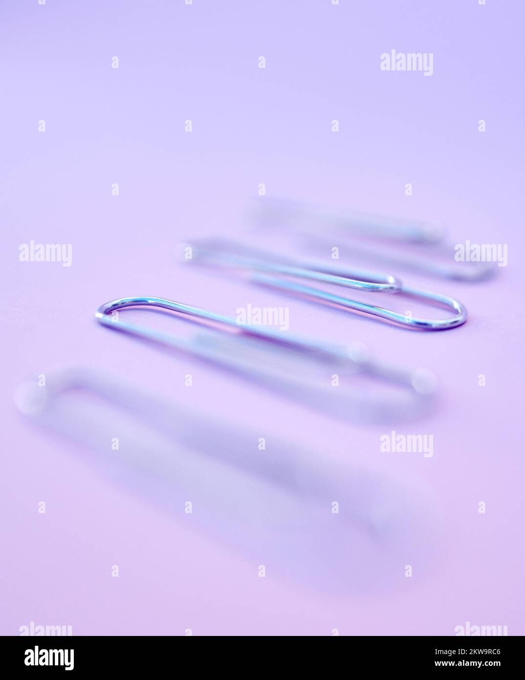 Row, graffette e cancelleria per ufficio per documenti in studio con sfondo viola. Forniture di lavoro, attrezzature e fermacavi in acciaio in una linea a. Foto Stock