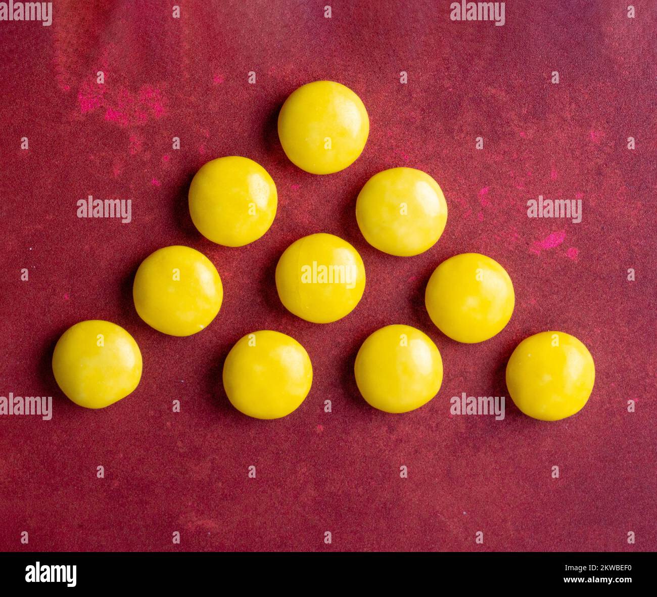 Ciottoli di cioccolato ricoperti di zucchero candito giallo brillante disposti in un triangolo su uno sfondo di borgogna Foto Stock