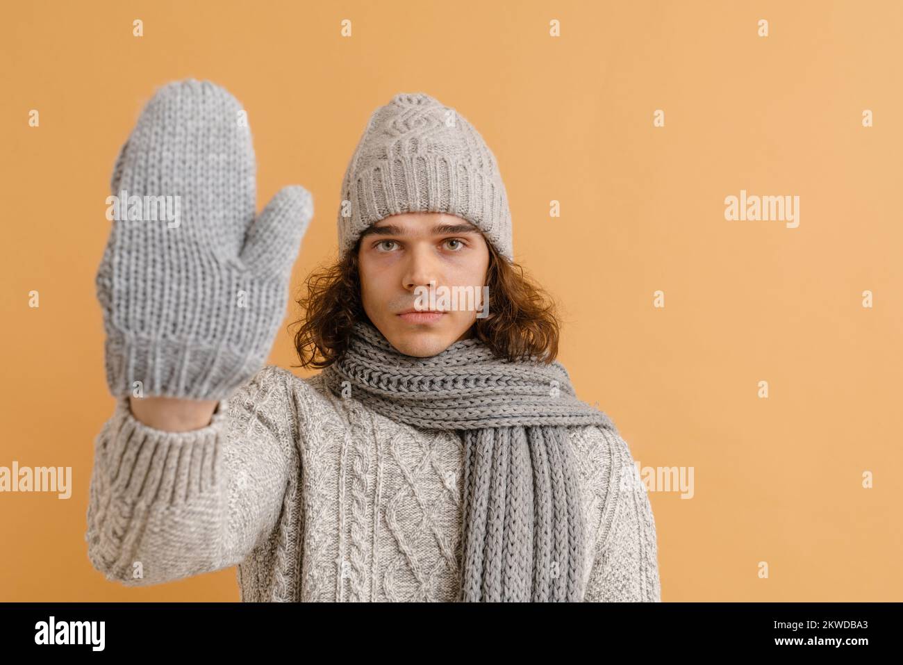 Giovane uomo bello con capelli lunghi in maglione e cappello invernale,  sciarpa e guanti che mostrano la sua palma su sfondo marrone isolato Foto  stock - Alamy