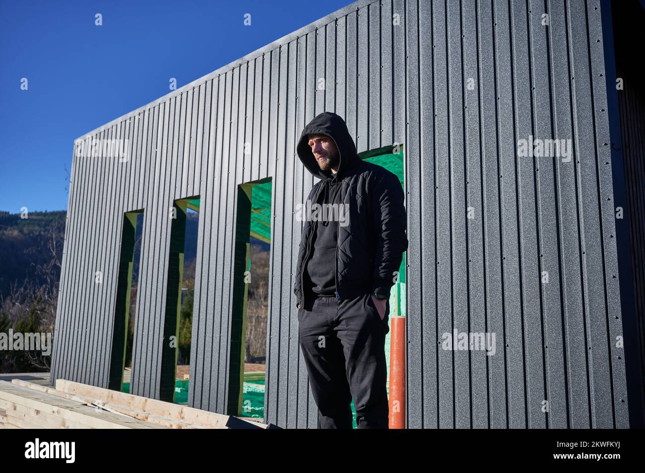 Ingegnere maschio costruzione casa con struttura in legno. Uomo in piedi sul cantiere, che ispeziona la qualità del lavoro. Foto Stock